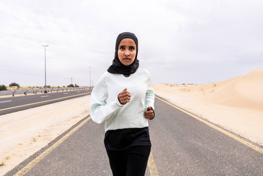Mooie Midden-Oosterse arabische vrouw draagt hijab training buiten in een woestijn - sportieve atletische moslim volwassen vrouw draagt burkini sportkleding doet fitness workout - Foto, afbeelding