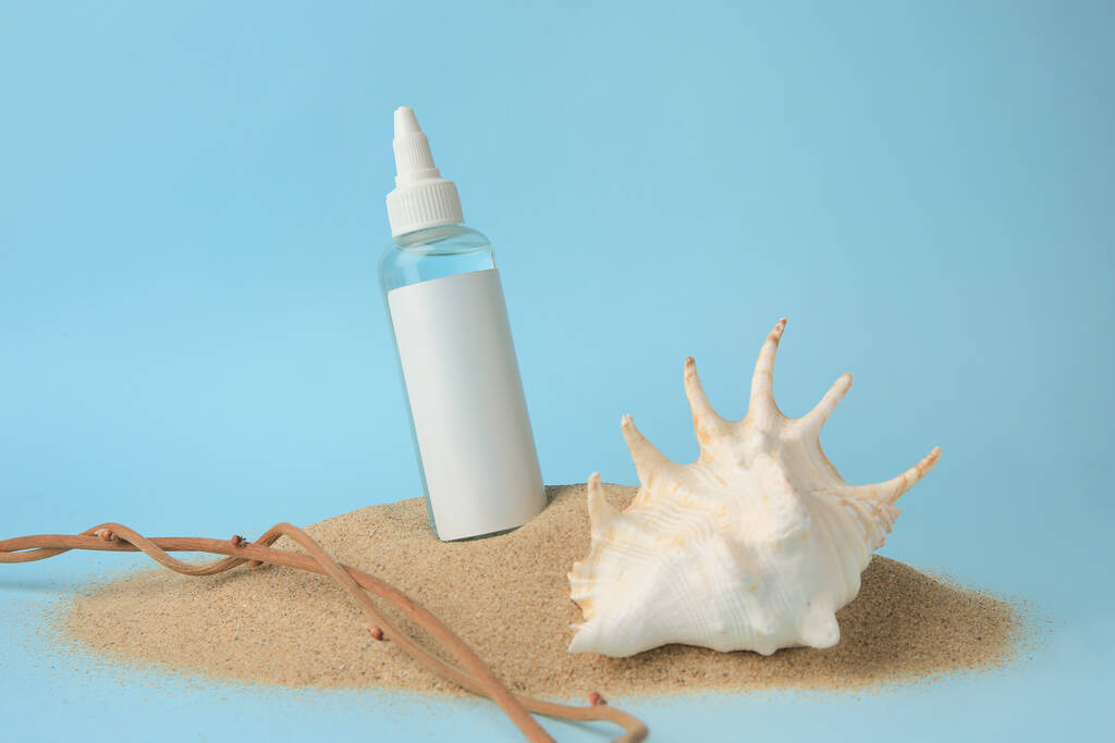 Botella con suero, concha y ramas sobre arena sobre fondo azul claro. Producto cosmético - Foto, imagen