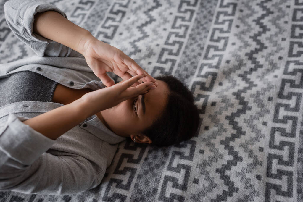 Wysoki kąt widzenia wielorasowej kobiety z depresją leżącej na łóżku w domu  - Zdjęcie, obraz