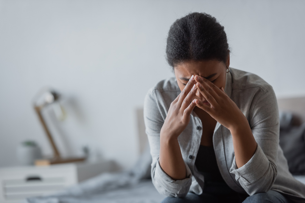 Traurige multirassische Frau berührt Gesicht, während sie im Schlafzimmer weint  - Foto, Bild