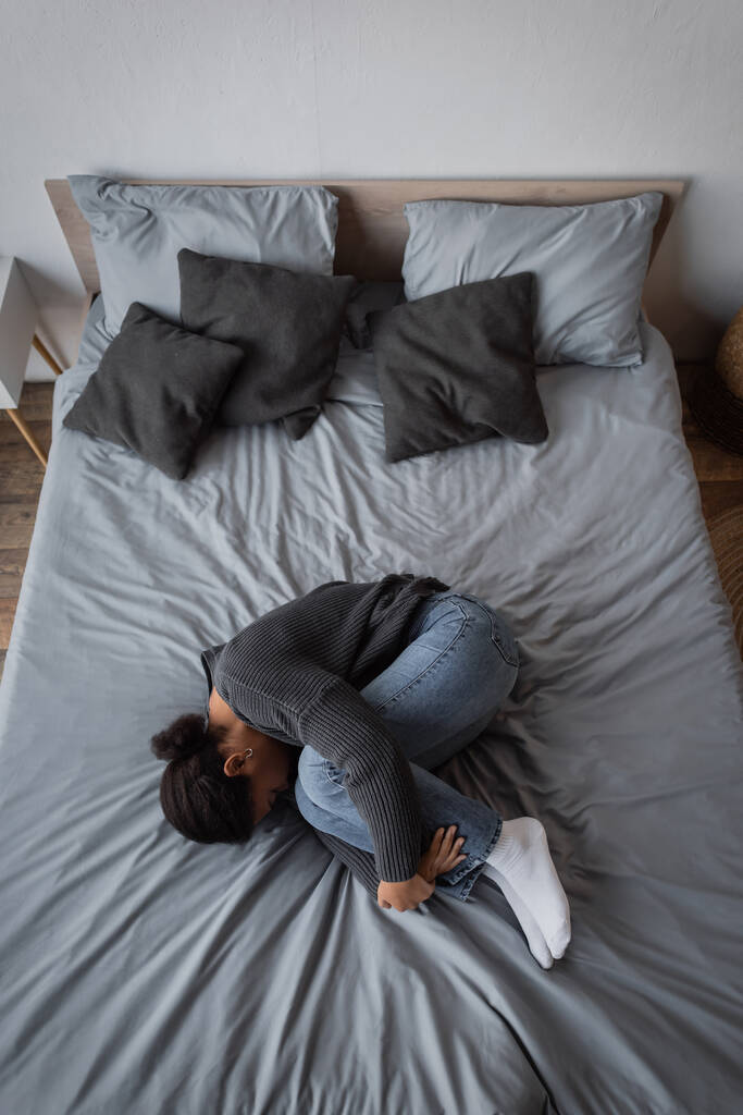 うつ病を持つ多人種女性のトップビューは自宅でベッドの上に横たわる  - 写真・画像