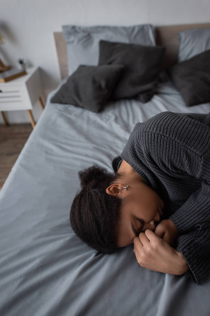 Depressive Frau in Strickpullover liegt auf Bett in verschwommenem Schlafzimmer  - Foto, Bild