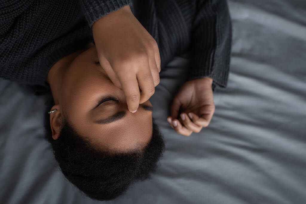 Vue du dessus de femme multiraciale frustrée touchant le visage tout en étant couché sur le lit  - Photo, image