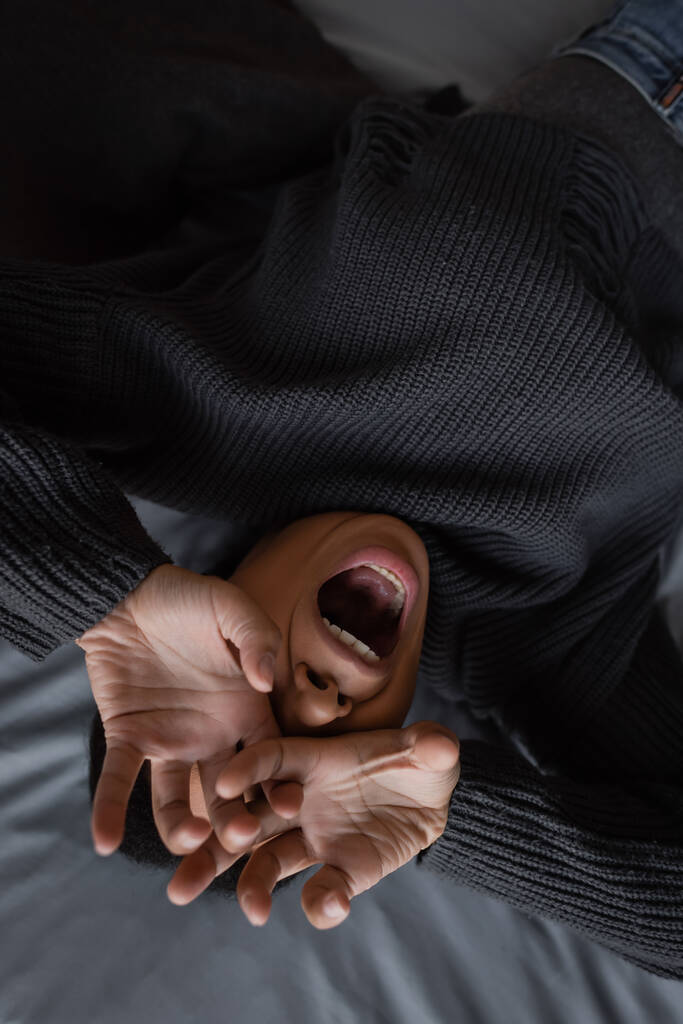 Top view of stressed multiracial woman covering face and screaming on bed at home  - Photo, Image