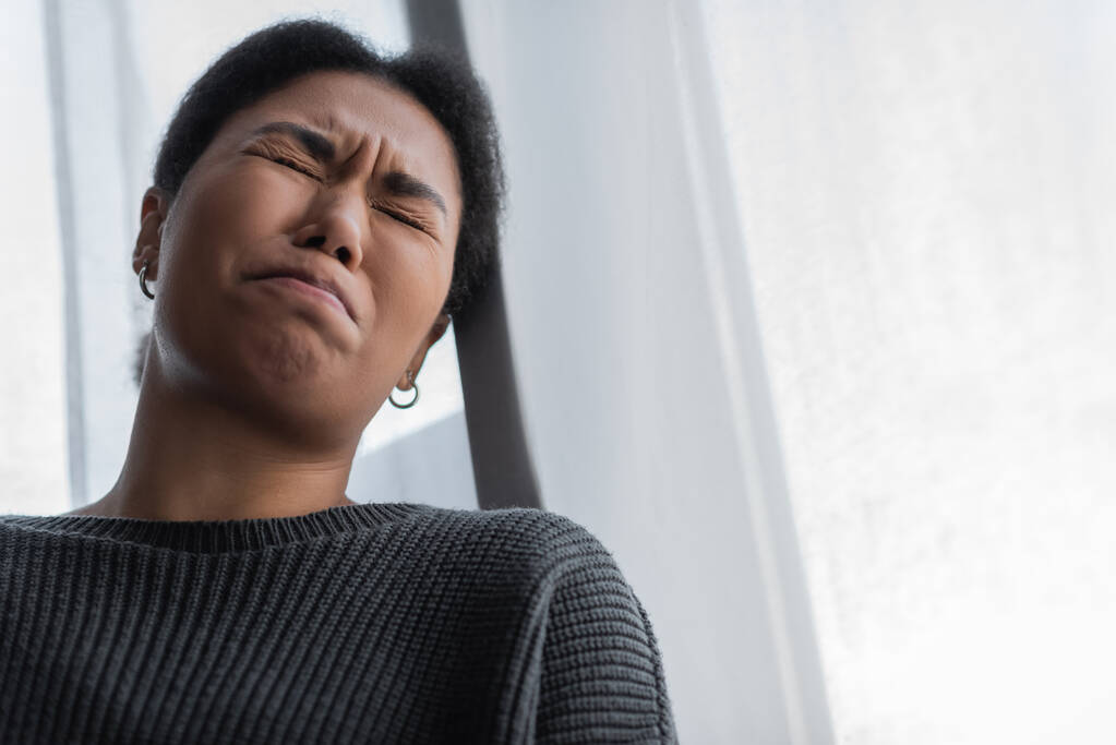 Lage hoek uitzicht van jonge multiraciale vrouw met depressie huilen thuis  - Foto, afbeelding