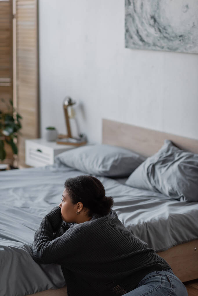Giovane donna multirazziale con problemi psicologici guardando lontano vicino a letto a casa  - Foto, immagini