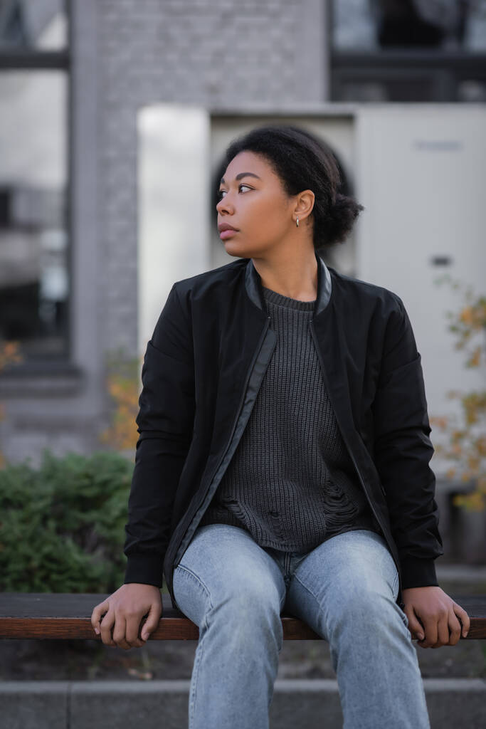 Kentsel sokakta bankta otururken ilgisiz bakışları olan çok ırklı bir kadın.  - Fotoğraf, Görsel