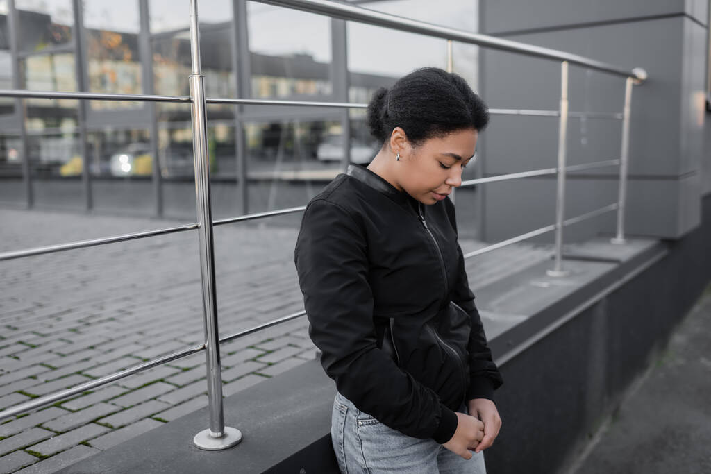 Junge multiethnische Frau mit Apathie steht in der Nähe von Gebäuden im Freien  - Foto, Bild