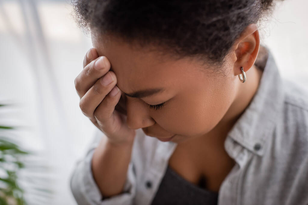 Enttäuschte multirassische Frau mit Angst, die zu Hause den Kopf berührt  - Foto, Bild