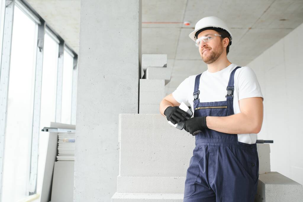 Porträt eines positiven, gut aussehenden jungen männlichen Bauunternehmers mit hartem Hut - Foto, Bild