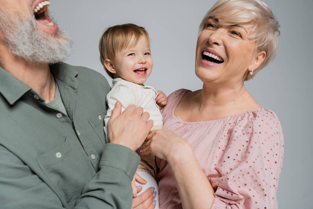 overjoyed couple laughing near beloved granddaughter isolated on grey - Photo, Image