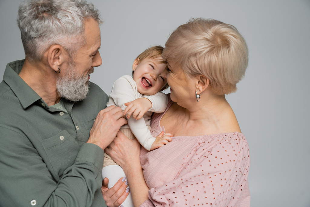 excited toddler girl laughing near happy grandparents isolated on grey - Photo, Image