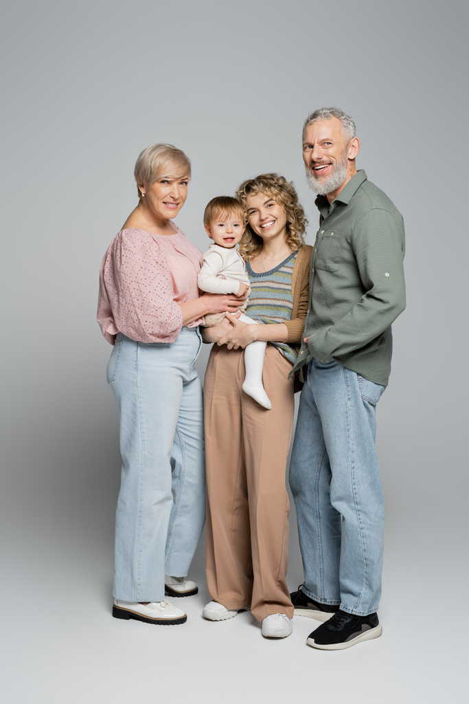 повна довжина щасливих бабусь і дідусів середнього віку і доросла дочка з дівчинкою, яка посміхається на камеру на сірому фоні
 - Фото, зображення