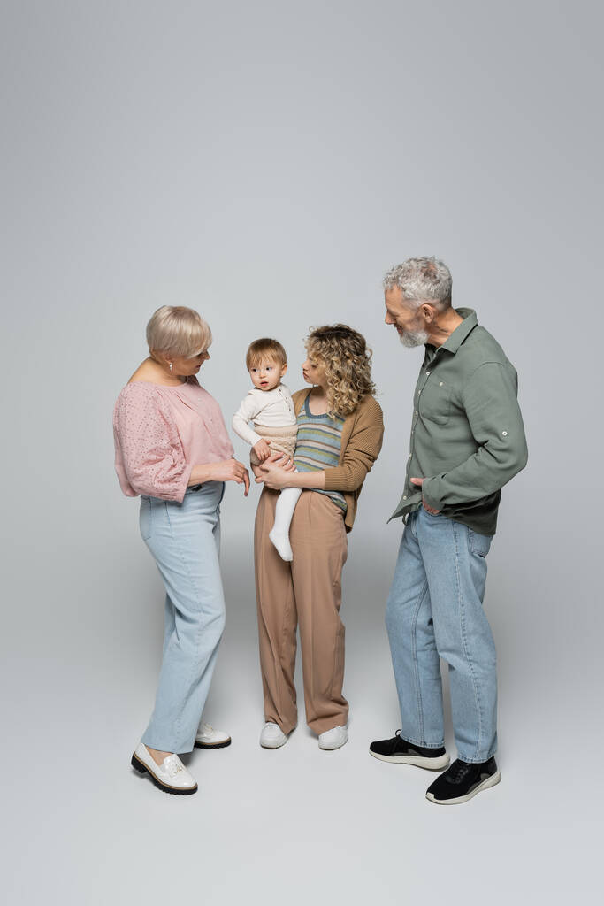 volledige lengte van de vrouw houden kleine dochter in de buurt gelukkig ouders op grijze achtergrond - Foto, afbeelding