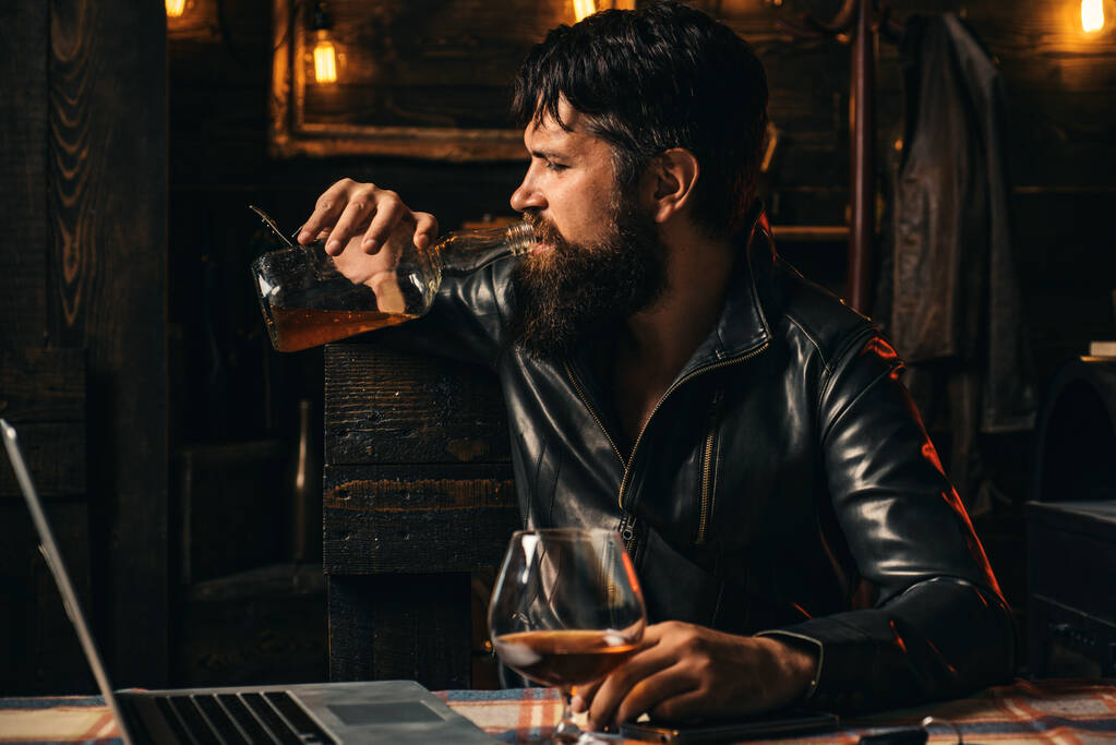El motociclista viene al bar. Un hombre frustrado con barba está bebiendo de una botella de whisky. Problemas en las relaciones. Alcoholismo, adicción al alcohol y concepto de personas - Foto, imagen