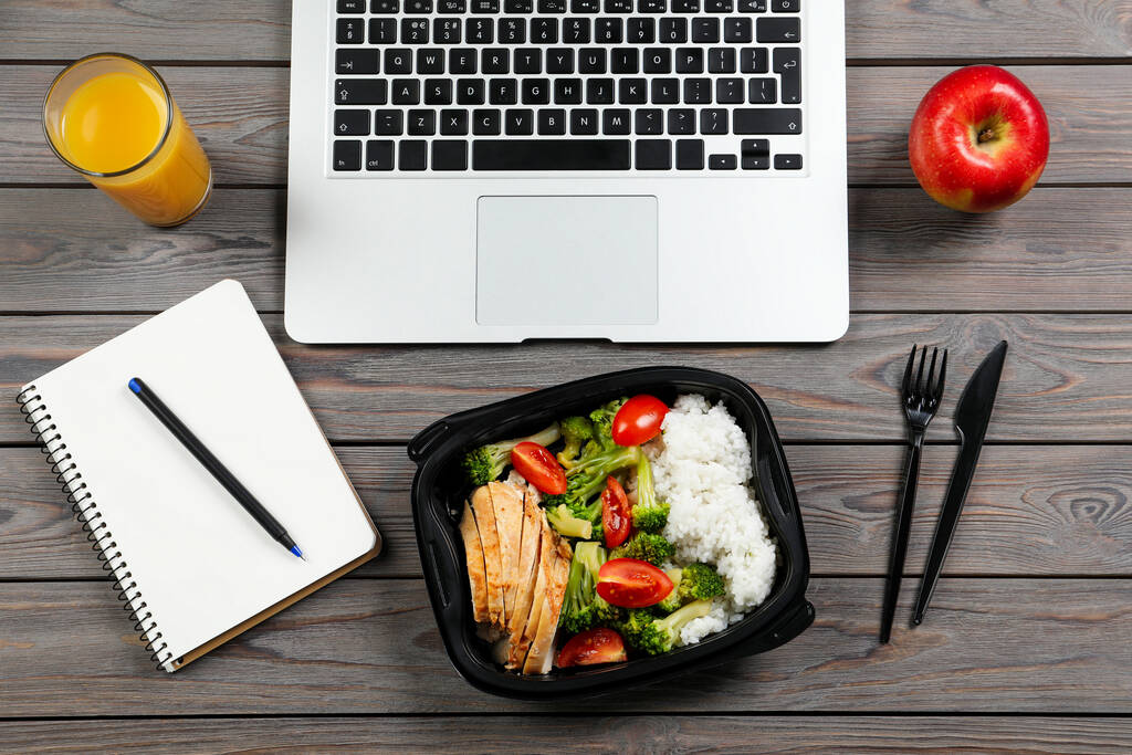 Kontejner s chutným jídlem, sklenicí džusu, laptopem a jablkem na dřevěném stole, plochý ležel. Pracovní oběd - Fotografie, Obrázek