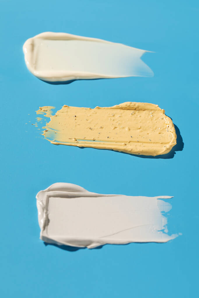 Δείγματα και υφές διαφόρων καλλυντικών για περιποίηση δέρματος και μαλλιών σε μπλε φόντο. Δείγματα. Φροντίδα δέρματος. - Φωτογραφία, εικόνα