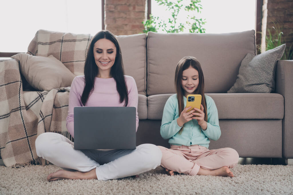 Фото позитивних користувачів сімейного гаджета мама дочка сидить на підлозі кімнати пошуку Wi-Fi на смартфоні нетбука
. - Фото, зображення