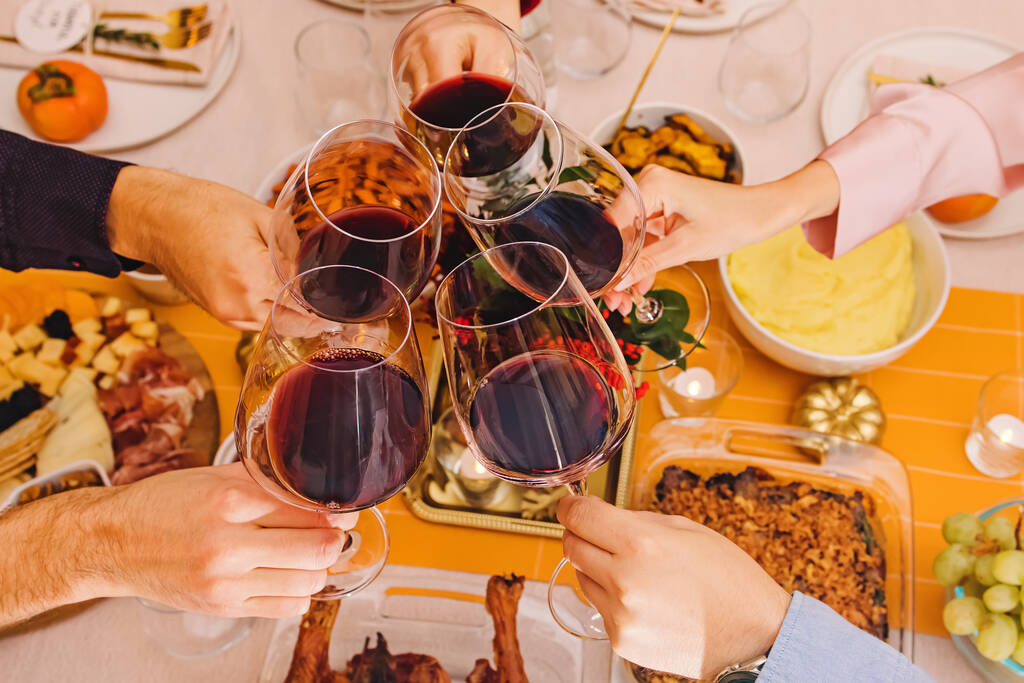 Las manos tintineando con unas copas llenas de vino tinto en la mesa de Acción de Gracias. Celebración, reunirse, Amistad - Foto, imagen