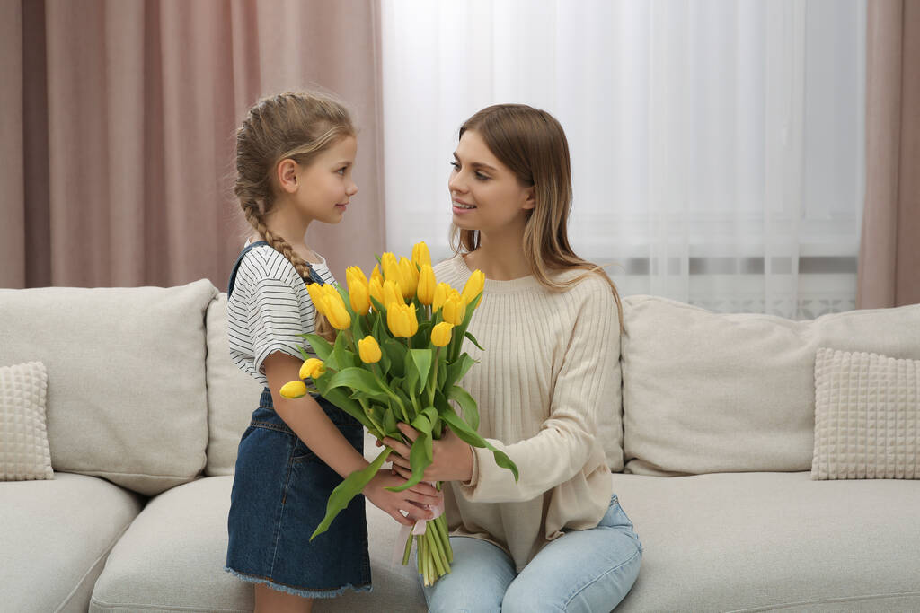 Malá dcerka blahopřeje mámě s kyticí žlutých tulipánů doma. Šťastný Den matek - Fotografie, Obrázek