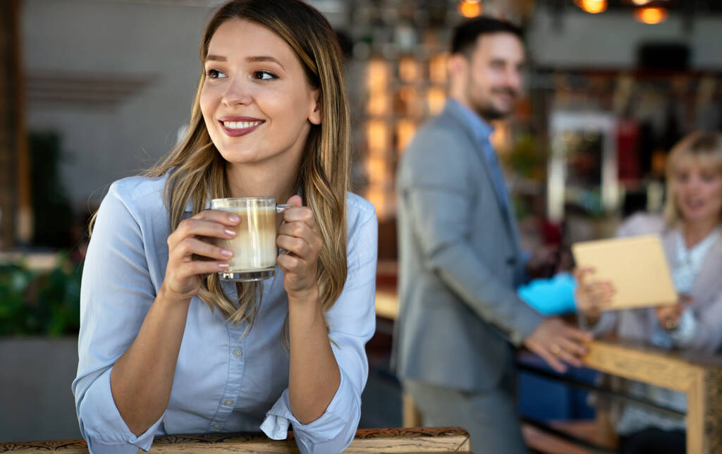 Πορτρέτο του ευτυχισμένη νεαρή επιτυχημένη επιχειρηματίας πίνοντας καφέ σε ένα διάλειμμα. Στο παρασκήνιο, οι συνάδελφοί της - Φωτογραφία, εικόνα