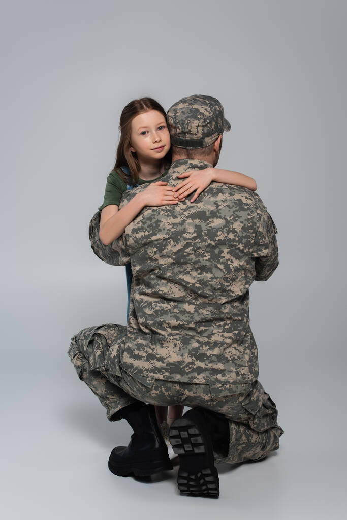 nastolatek dziecko przytulanie żołnierz w wojskowym mundurze podczas dzień pomnik na szary  - Zdjęcie, obraz