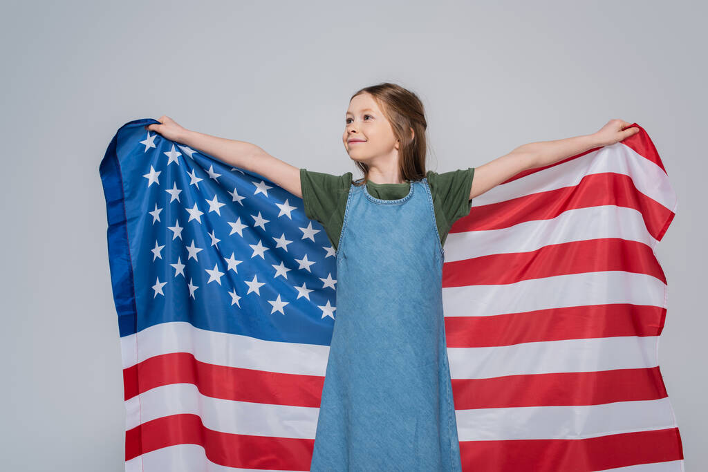 patriotyczne nastolatka dziewczyna uśmiech a trzymając ogromny flaga Ameryka podczas pamiątkowy dzień izolowany na szary  - Zdjęcie, obraz