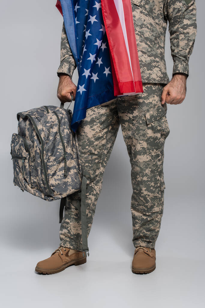 Перевернутий вид армійського солдата у формі з прапором Сполучених Штатів Америки, який тримає рюкзак на сірому  - Фото, зображення