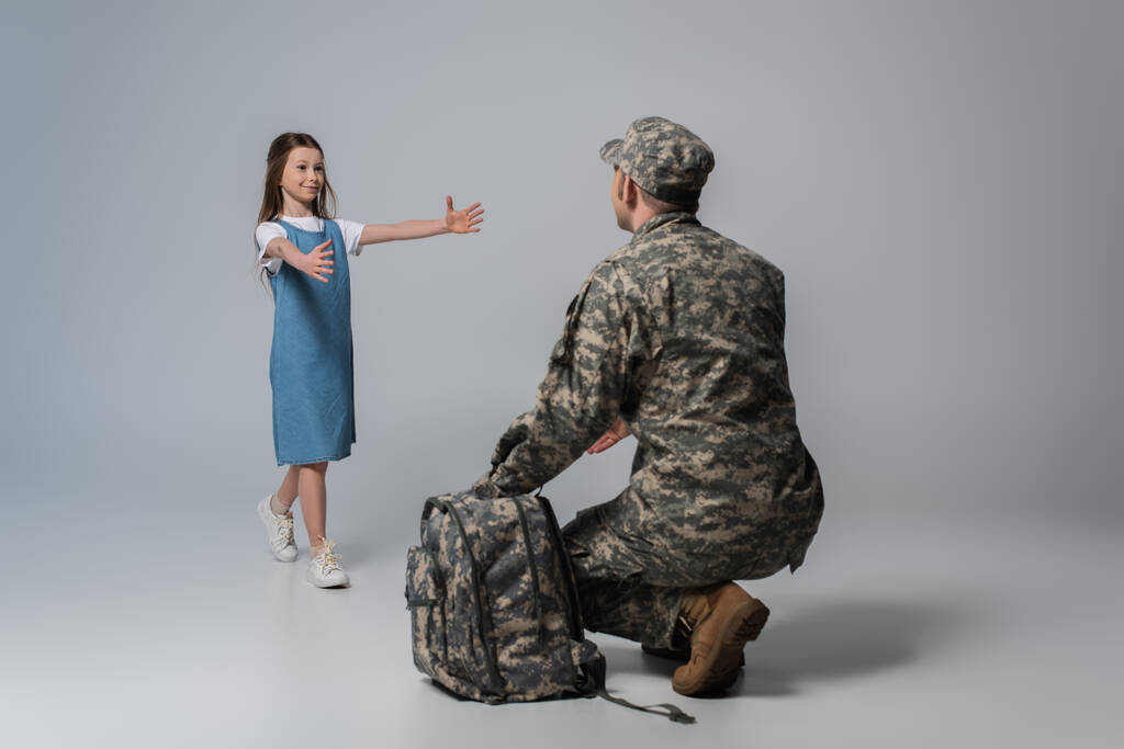 bambino felice benvenuto padre in uniforme militare durante il ritorno a casa su sfondo grigio - Foto, immagini
