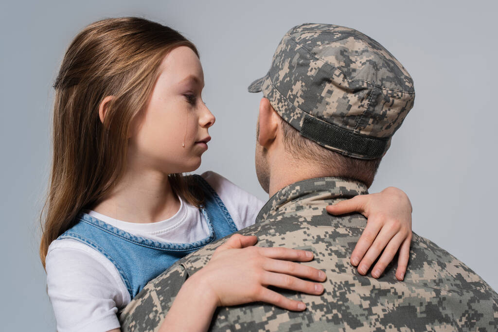patriotic girl looking at father in army uniform and crying during memorial day isolated on grey - Photo, Image