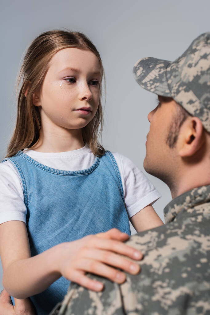 Patriotisches Mädchen sieht Soldat in Armeeuniform an und weint am Gedenktag, isoliert auf grau - Foto, Bild