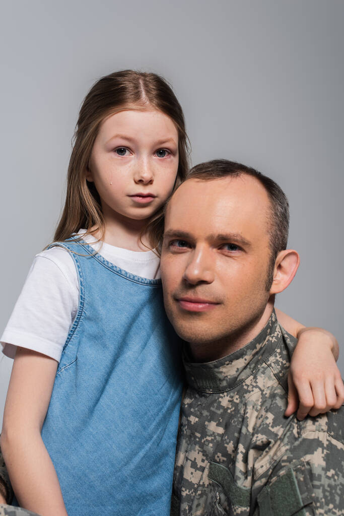 patriotyczne dziecko przytula żołnierza w mundurze wojskowym i płacze w dzień pamięci odizolowany na szarości - Zdjęcie, obraz
