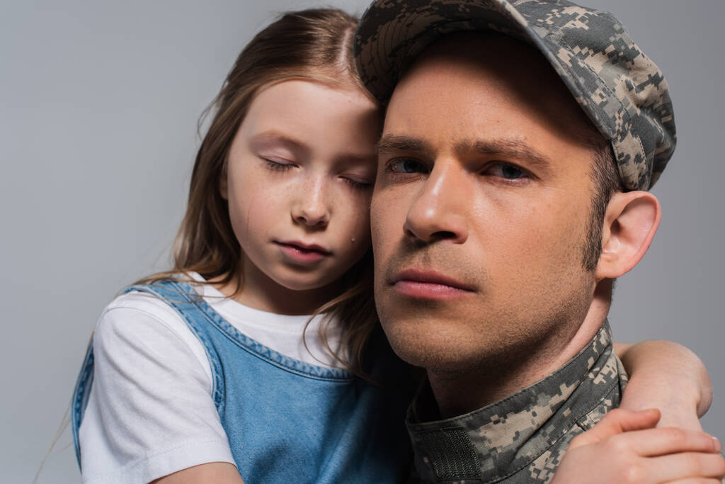 triste chica abrazando padre en uniforme militar y llorando durante el día conmemorativo aislado en gris - Foto, Imagen