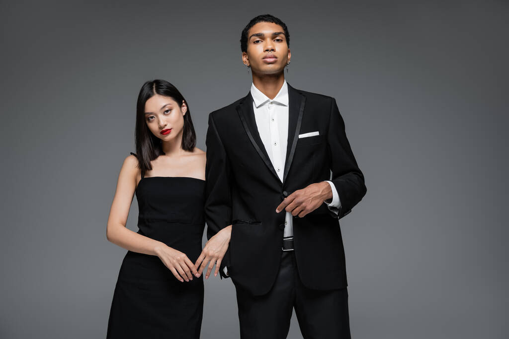 jovem casal interracial no elegante desgaste formal olhando para a câmera isolada no cinza - Foto, Imagem