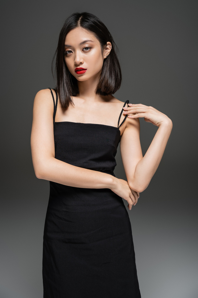charming asian woman in black elegant dress looking at camera on grey background - Photo, Image
