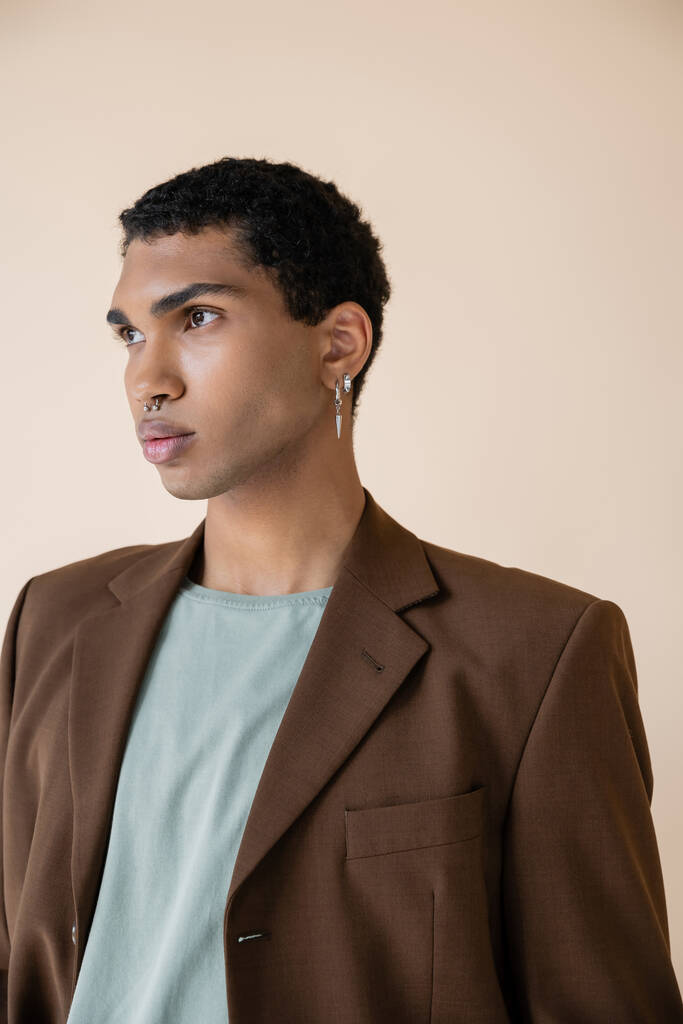 jovem e elegante homem afro-americano com piercing prata olhando para longe isolado no bege - Foto, Imagem