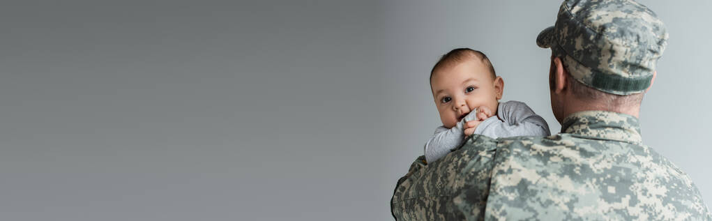 militar con uniforme militar y gorra abrazando al hijo recién nacido aislado en gris, pancarta  - Foto, imagen