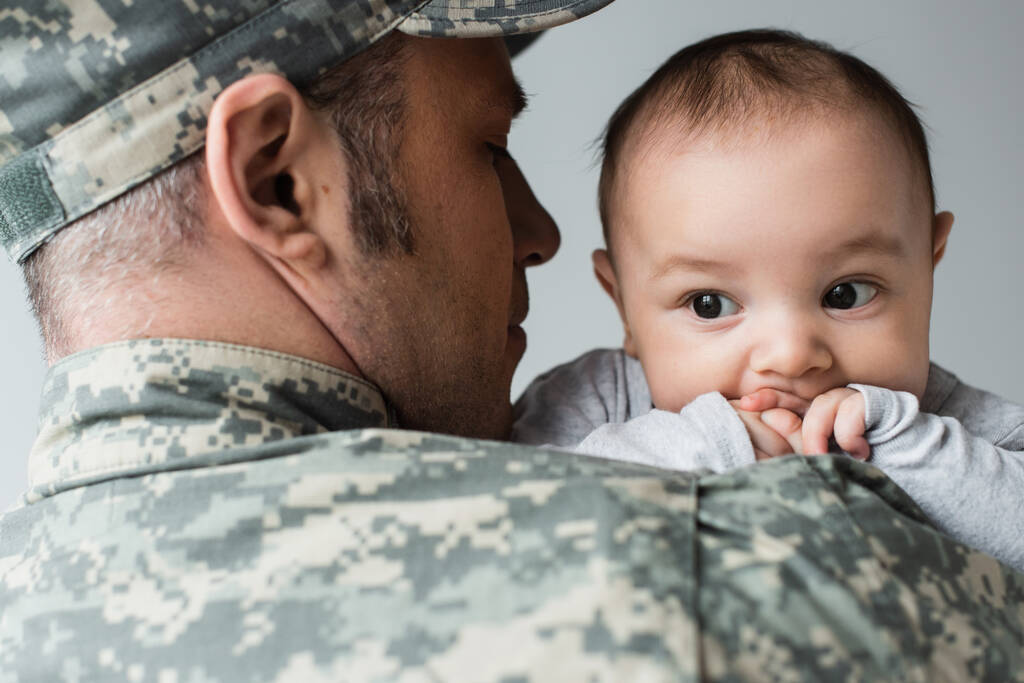 homem de uniforme militar e boné abraçando filho recém-nascido isolado em cinza  - Foto, Imagem