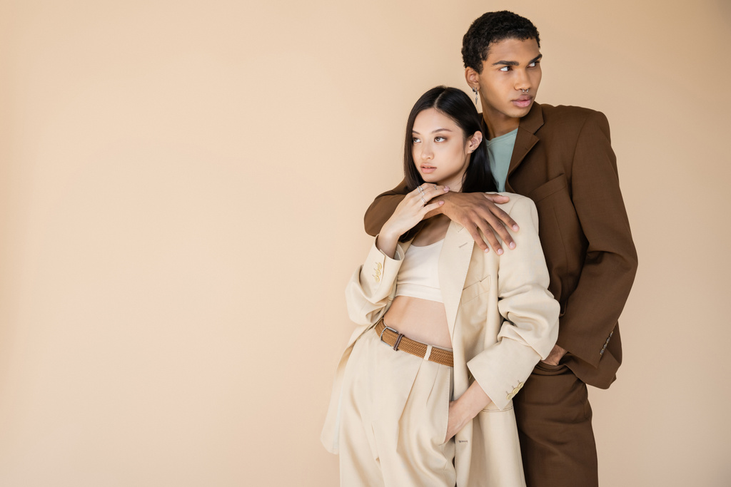stylish african american guy hugging young asian woman and looking away isolated on beige - Photo, Image