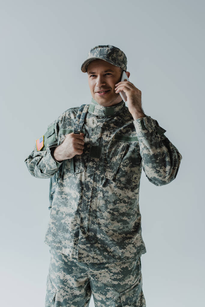 boldog katona katonai egyenruhában beszél okostelefonon elszigetelt szürke  - Fotó, kép