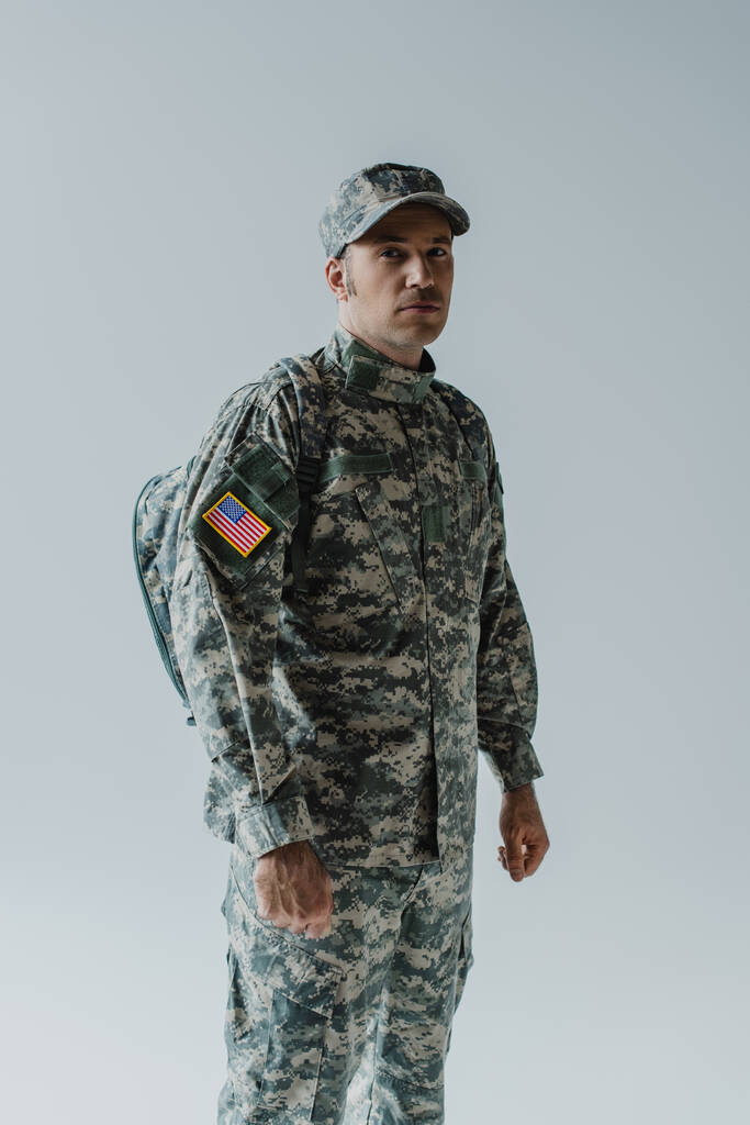 Soldado americano en uniforme del ejército con bandera nacional de pie aislado en gris  - Foto, Imagen