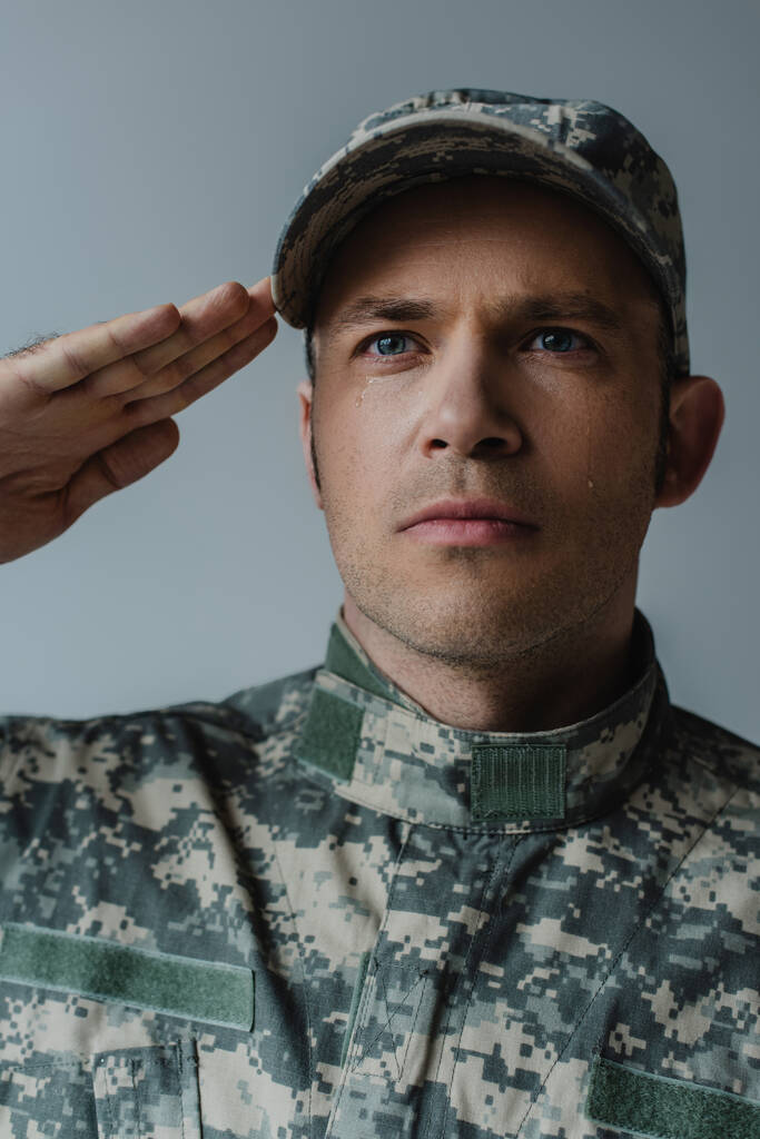 sad soldier in military uniform crying and saluting during memorial day isolated on grey  - Photo, Image