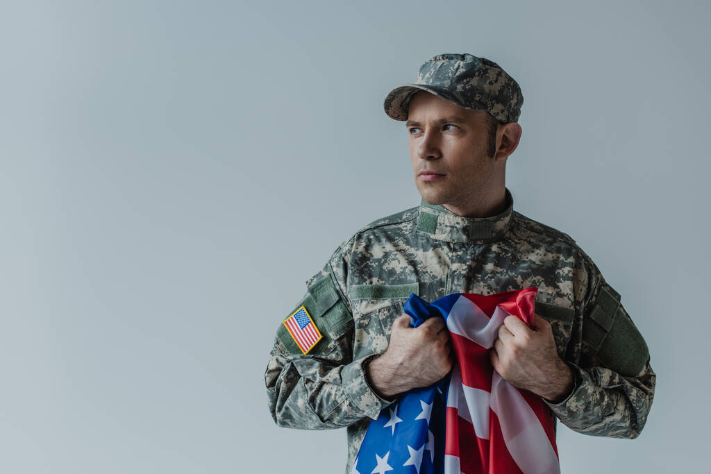 Amerikaanse soldaat met vlag van de Verenigde Staten tijdens het huilen tijdens herdenkingsdag geïsoleerd op grijs  - Foto, afbeelding