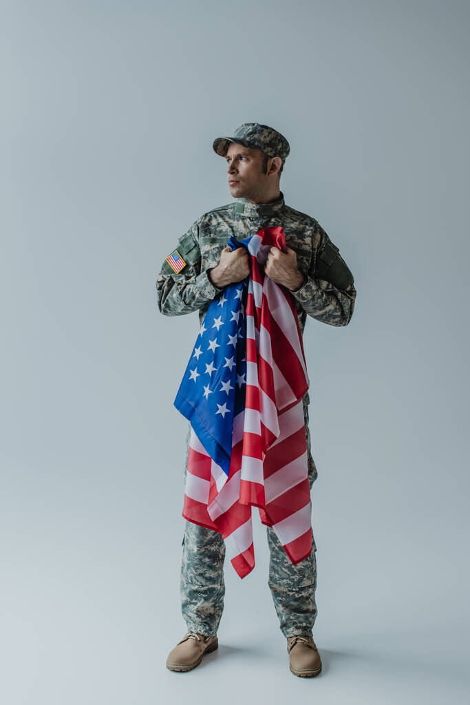 toute la longueur du soldat américain tenant le drapeau des États-Unis pendant la journée commémorative sur gris  - Photo, image