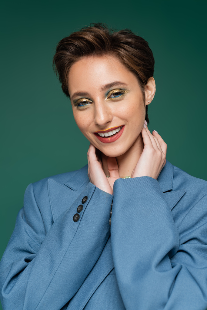 smiling young woman with short hair posing in blue suit on turquoise green background  - Photo, Image