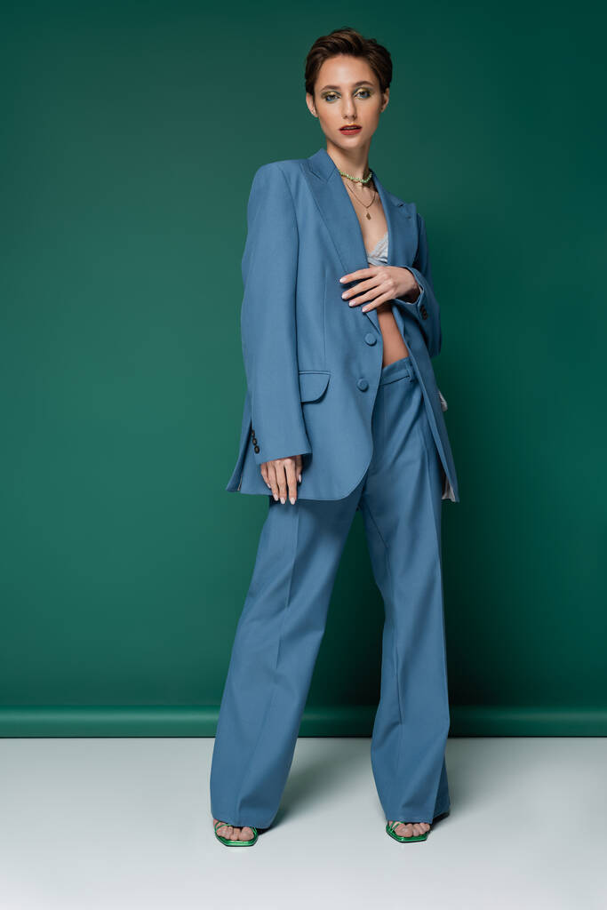volledige lengte van jong model met kort haar poseren in blauw pak op turquoise witte achtergrond  - Foto, afbeelding