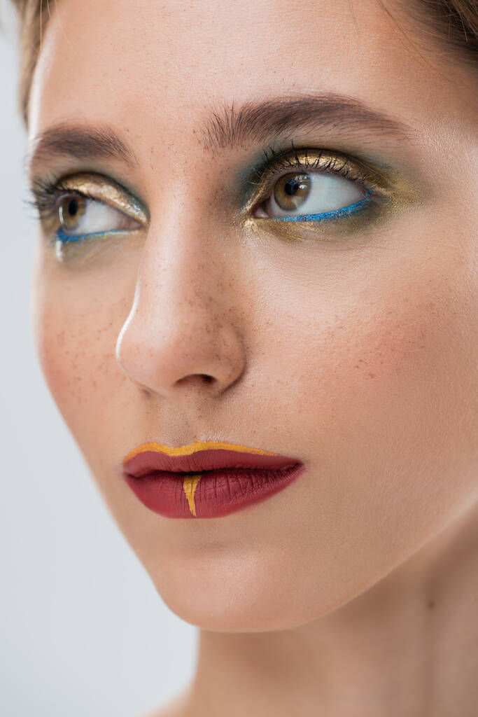 Nahaufnahme einer jungen Frau mit glänzendem Augen-Make-up und roten Lippen isoliert auf grau - Foto, Bild