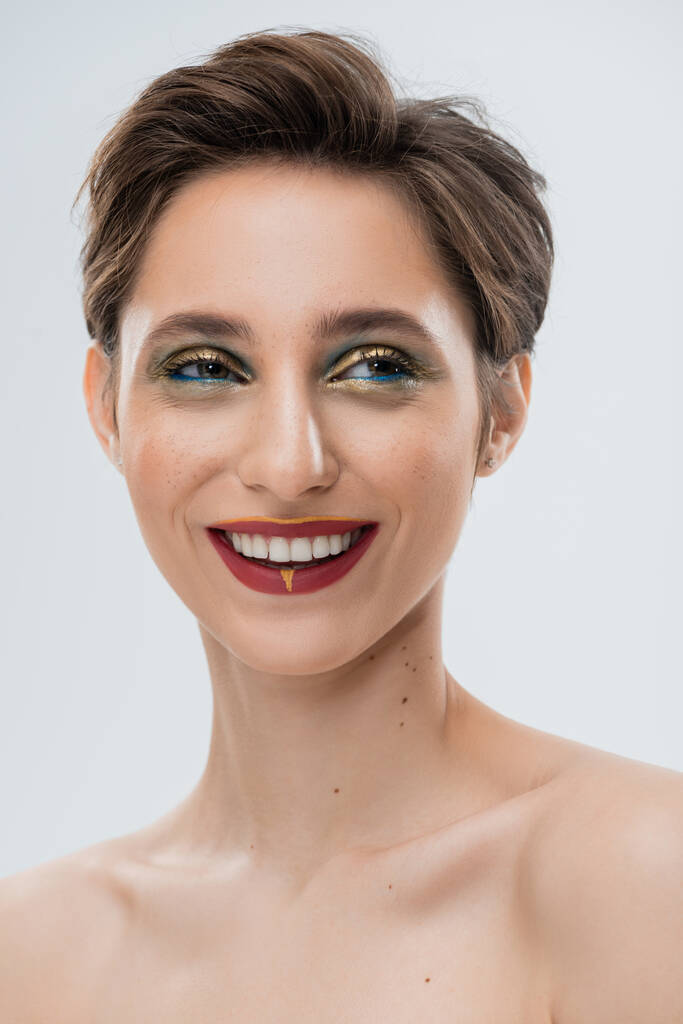 портрет веселої молодої жінки з блискучим макіяжем і коротким волоссям ізольовані на сірому
  - Фото, зображення