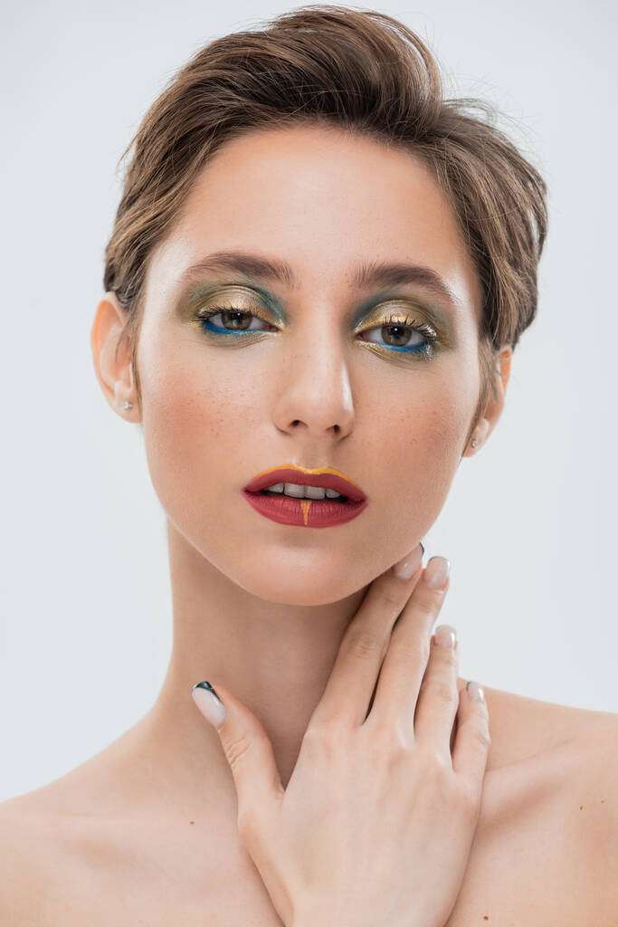 brunette young woman with shimmery eye makeup and red lips touching neck isolated on grey  - Photo, Image