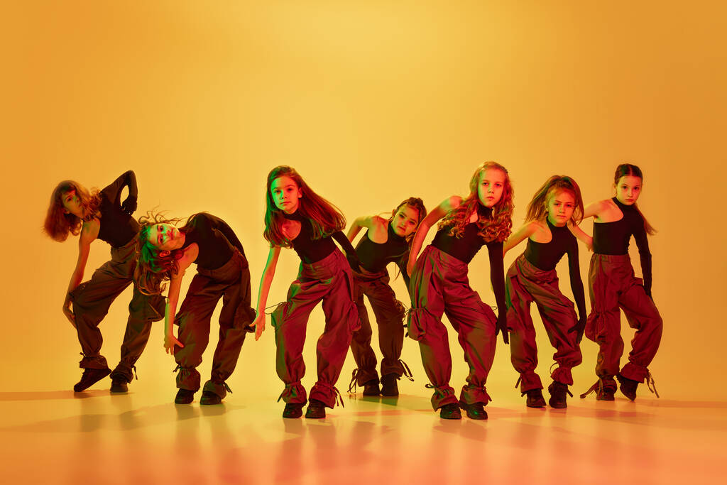 Výrazný tanec. Skupina stylových holčiček, děti, tanec, trénink hip-hop na žlutém pozadí studia v neonovém světle. Pojem dětství, hobby, sportovní životní styl, vzdělání - Fotografie, Obrázek